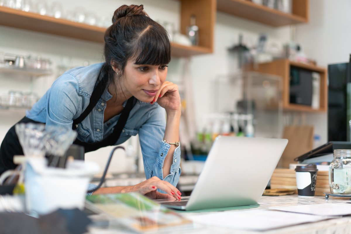 A small business owner reviewing a funding application on a laptop at her counter